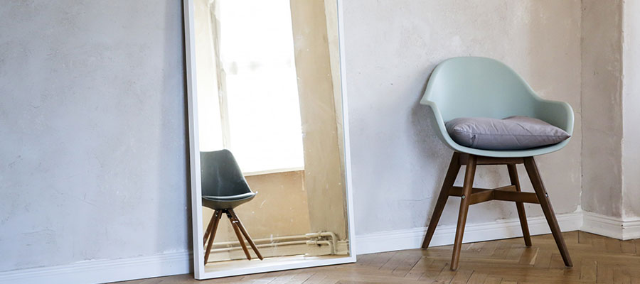 Ein Stuhl und ein Spiegel mit Wand in Betonoptik im Hintergrund.