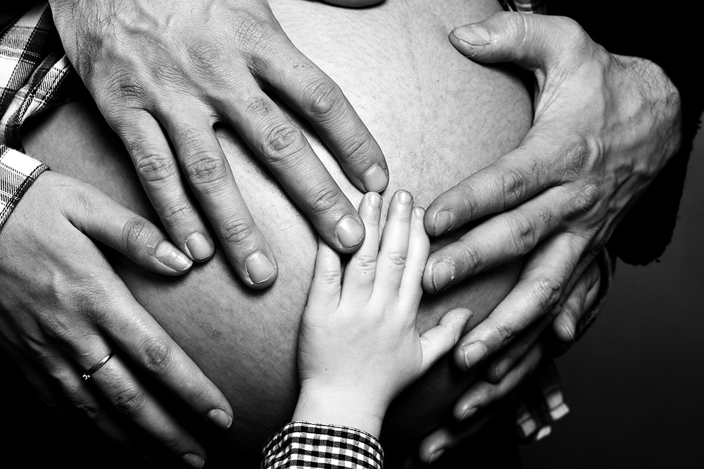 Ganze Familie fasst mit Händen Babybauch an.
